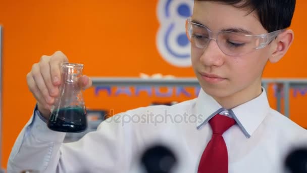 Colegial en la clase de química de la escuela mirando en el tubo de ensayo, haciendo experimentos . — Vídeo de stock