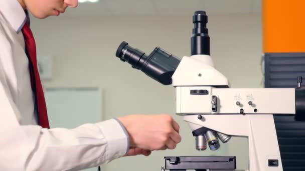 Adolescente en el laboratorio de la escuela estudiando biología, mirando a través del microscopio . — Vídeo de stock