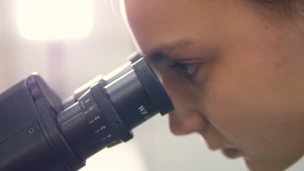 Σχολείο κορίτσι ψάχνει σε μικροσκόπιο. Γκρο πλαν. — Αρχείο Βίντεο