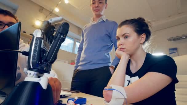 Deux scientifiques et une femme handicapée surprise regardent le bras du robot, qui bouge ses meneurs selon le souhait des dames . — Video