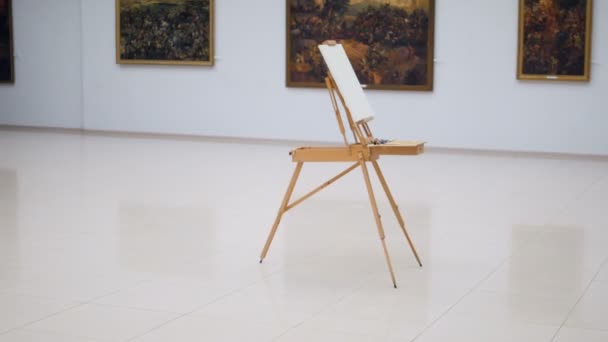 The steadicam shooting of the easel with white canvas on it. It is standing in the center of the gallery. 4K. — Stock Video