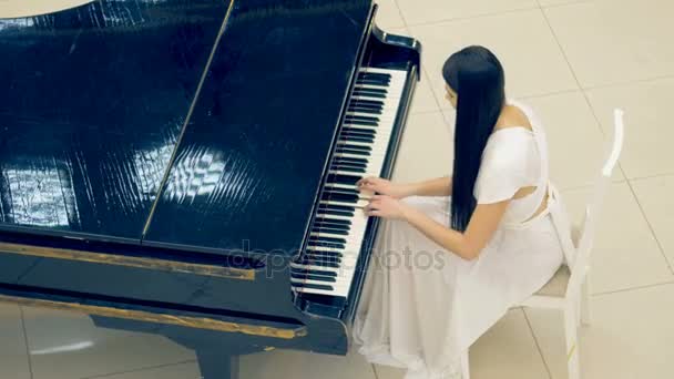 Красивая девушка играет на пианино в белом платье — стоковое видео