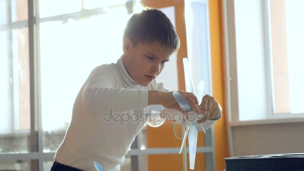 Un niño estudiando un pequeño modelo de turbina eólica . — Vídeo de stock