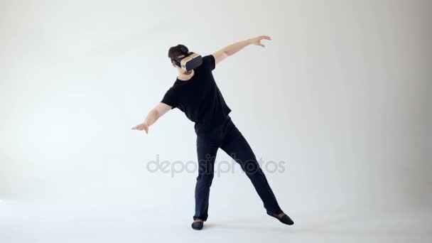 Un hombre está usando auriculares de realidad virtual dando pasos cuidadosos. Fondo blanco. 4K . — Vídeos de Stock