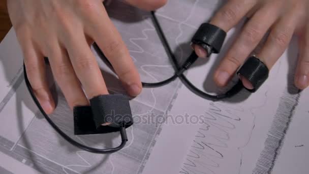 Hands with finger sensors lying above polygraph printouts. 4K 60 fps. — Stock Video