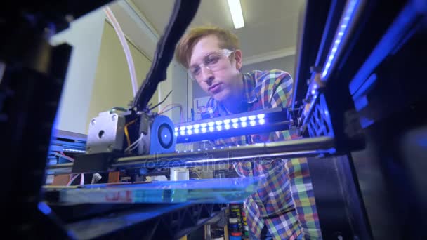 Bajo ángulo del hombre observando el proceso de impresión en una impresora 3D. 4K . — Vídeos de Stock