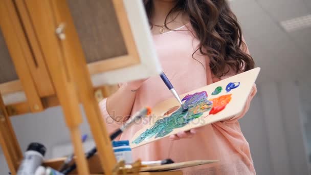 Κοπέλα που κρατά μια βούρτσα, ανάμειξη χρωμάτων για την εικόνα της. — Αρχείο Βίντεο