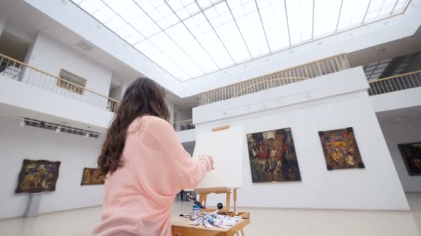 Kvinnlig konstnär målar en bild i galleriet. — Stockvideo