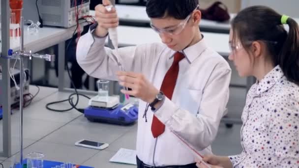 Un colegial demuestra cómo agregar químicos en un tubo . — Vídeo de stock