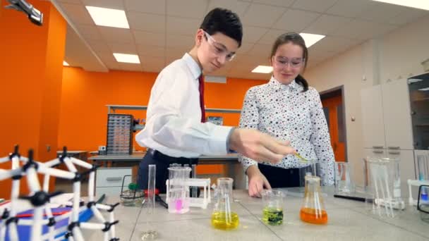 Ein Mädchen beobachtet einen Jungen beim Mischen von Chemikalien. — Stockvideo