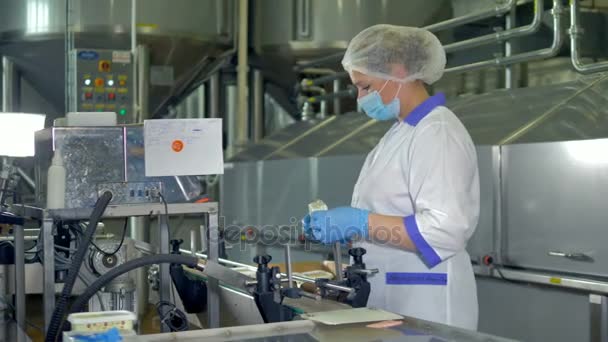 A factory operator in a plastic cap and a mask checks cheese packages. 4K. — Stock Video