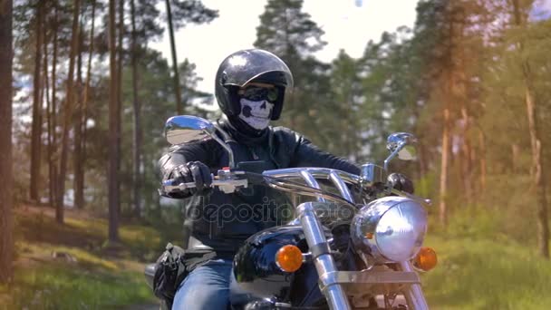 Retrato. Un hombre con una máscara de cráneo se sienta en una bicicleta . — Vídeos de Stock