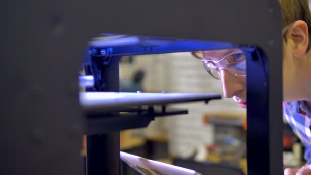 Ingenjör i skyddsglasögon styr den första etappen av ett Fdm-utskrift. 4k. — Stockvideo