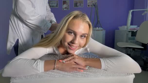 Una mujer rubia sonríe en una mesa de masaje . — Vídeo de stock