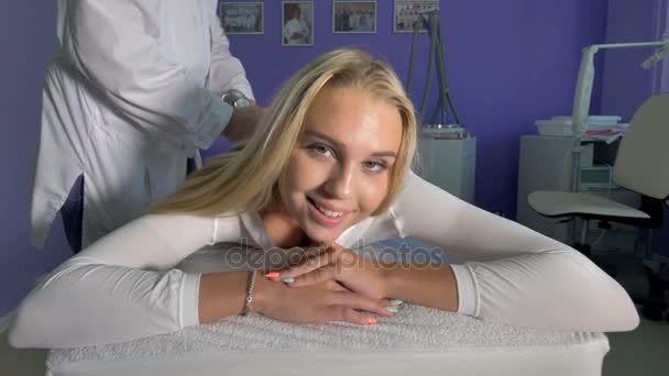 En blond kvinna ler på en massagebänk. — Stockvideo