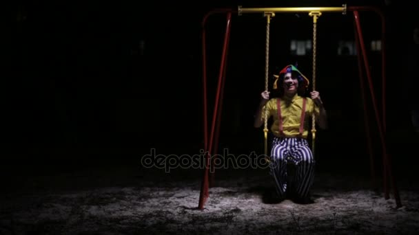 Клоун їде низькими дитячими гойдалками в темряві . — стокове відео