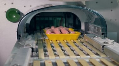 Sosis basamaklı bir konveyör hattı üzerinde sarı tepsiler.