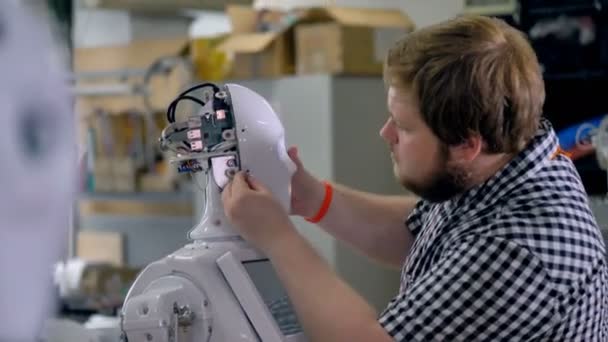 Een man hecht schroeven op een hoofd shell van robots. — Stockvideo