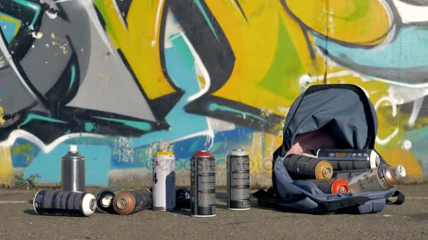 Latas de pintura en aerosol usadas en una mochila cerca de una pared de graffiti . — Vídeo de stock