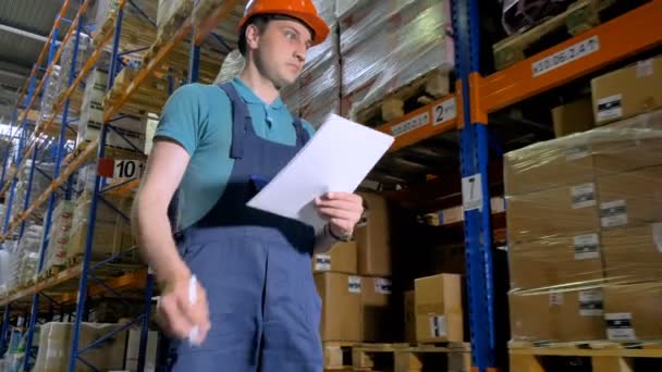 A young warehouse worker walks and takes note on paper. — Stock Video