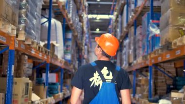 Depo rafları kadar arayan bir işçisi arkadan görünüm.