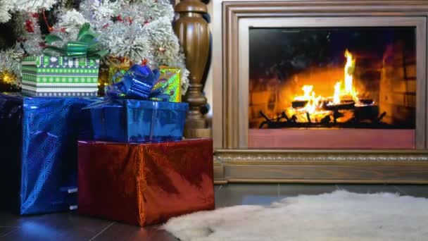 Kerstcadeautjes naast een brandende open haard. Kerstmis achtergrond. — Stockvideo