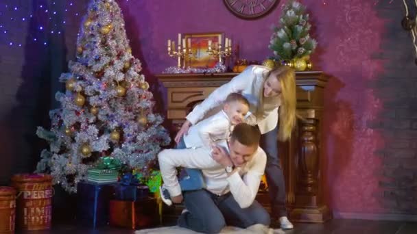 Una familia con un niño pequeño juega al lado de un árbol de Navidad . — Vídeo de stock