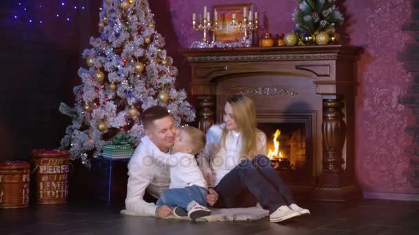 Un niño besa la cara de los padres cerca de un árbol de Navidad . — Vídeos de Stock