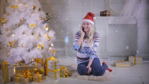 Μια νεαρή γυναίκα μιλά στο τηλέφωνό της κάτω από ένα χριστουγεννιάτικο δέντρο. — Αρχείο Βίντεο
