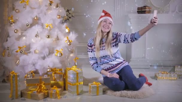 Een jonge vrouw neemt een selfie onder een kerstboom. — Stockvideo