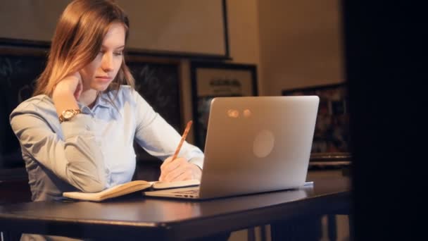 Attraktiv dam sitter på den bärbara datorn och göra anteckningar. Porträtt. HD. — Stockvideo