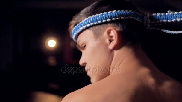Una vista posteriore su un combattente Muay Thai uomo con un cerchietto intrecciato a piedi sul ring di combattimento . — Video Stock