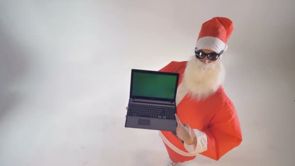 Santa Claus hält einen Laptop mit grünem Bildschirm in der Hand und schätzt ihn. — Stockvideo