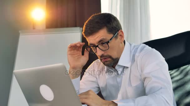 Un hombre de negocios cansado escribe en un portátil . — Vídeo de stock