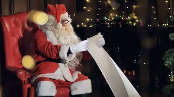 Santa en su silla cerca del árbol de Navidad lectura de la lista de regalos de año nuevo . — Vídeo de stock