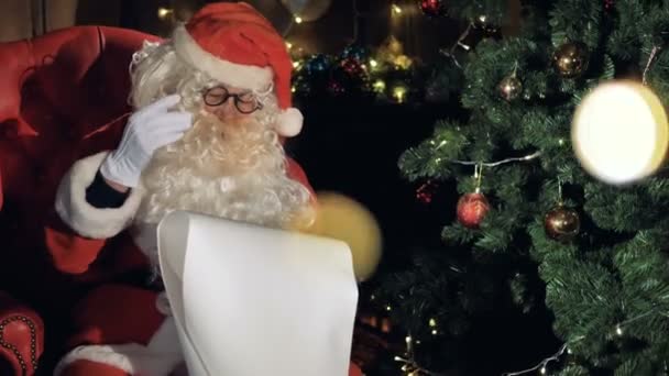 Nahaufnahme Weihnachtsmann in der Nähe geschmückten Weihnachtsbaum Leseliste mit Weihnachtswünschen. — Stockvideo
