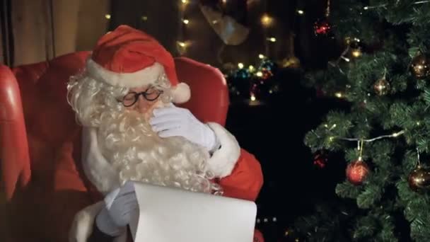 Santa in de buurt van de kerstboom lezen Nieuwjaar cadeau lijst. — Stockvideo