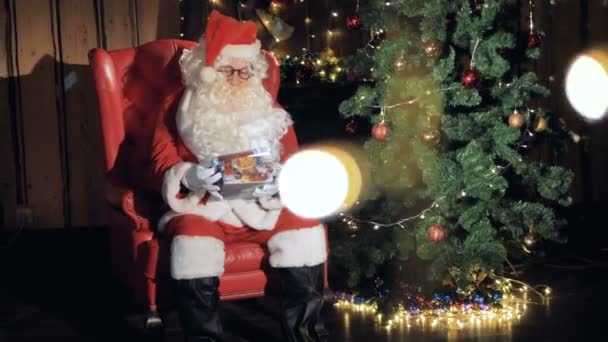 Santa opens christmas gist near christmas fireplace. 4K. — Stock Video