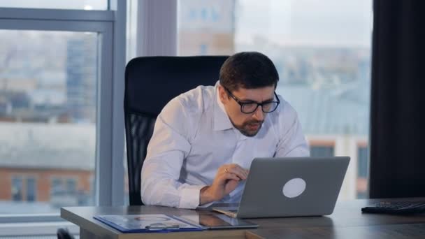 A smiling businessman works on a laptop and yawns. — Stock Video