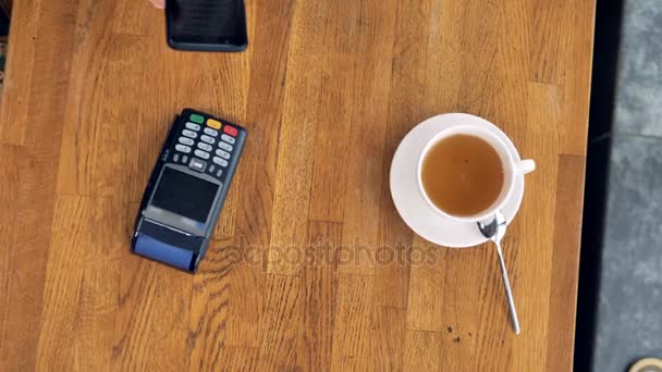 Ein Blick von oben auf eine Kaffeetasse und ein Smartphone während einer nfc-Zahlung. — Stockvideo