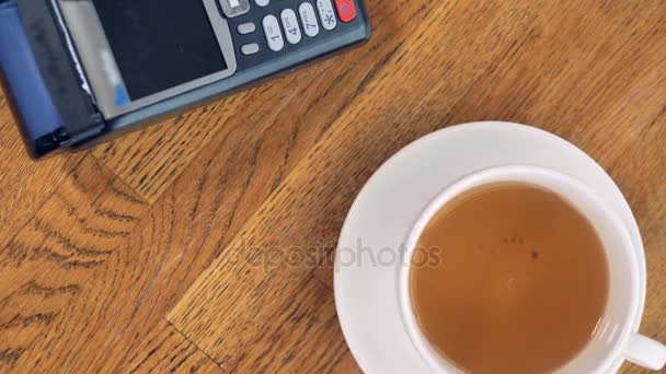 An extreme close-up on a latte cup an NFC terminal with a smartphone. — Stock Video