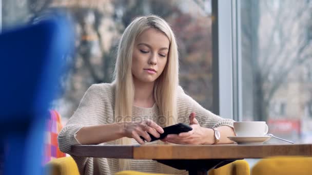 En blond tjej blir ledsen efter att titta på sin smartphone. — Stockvideo