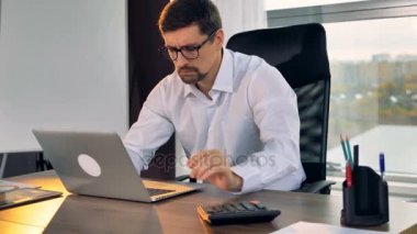 Bir işadamı bir Resepsiyon hesap makinesi diz üstü kullanır..