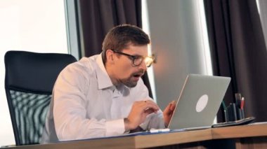 Bir işadamı bir dizüstü bilgisayarda türleri ve mutlulukla gülümsüyor.