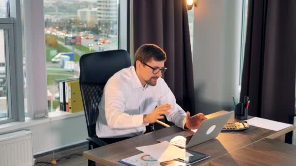Een zakenman typt op een laptop en vernietigt papier in frustratie. — Stockvideo