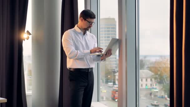 Un hombre de negocios está cerca de una ventana alta y tipos . — Vídeos de Stock