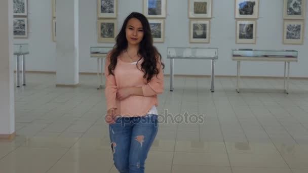 La foto steadicam di una giovane ragazza che cammina lungo la galleria e viene al cavalletto. 4K . — Video Stock