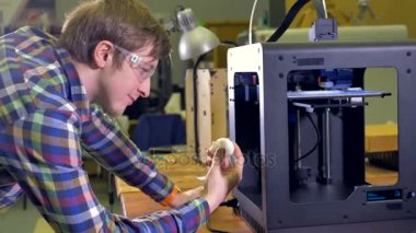 Mutlu bir mühendis bir beyaz prototip kafa tutan ve bir çalışma 3d yazıcıda görünüyor. 4k.