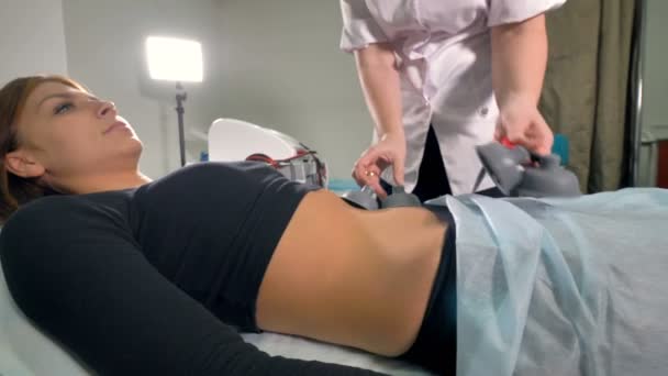 Un médico coloca electrodos de vacío en el abdomen de las mujeres . — Vídeos de Stock