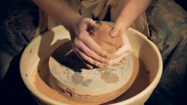 Potters handen vorm brokken klei over een wiel. — Stockvideo